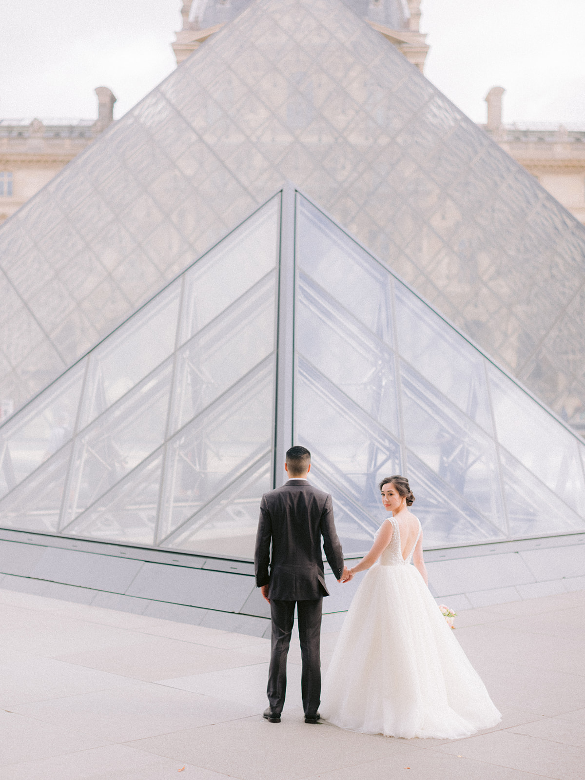 They are walking and in front of them is the Louvre Pyramid